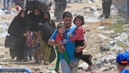 A Syrian refugee carrying children, walks in Turkey, in Akcakale, southeastern Turkey, as he and others flee intense fighting in northern Syria between Kurdish fighters and Islamic State militants, Monday, June 15, 2015. The flow of refugees came as Syrian Kurdish fighters closed in on the outskirts of a strategic Islamic State-held town on the Turkish border. (AP Photo/Lefteris Pitarakis)
